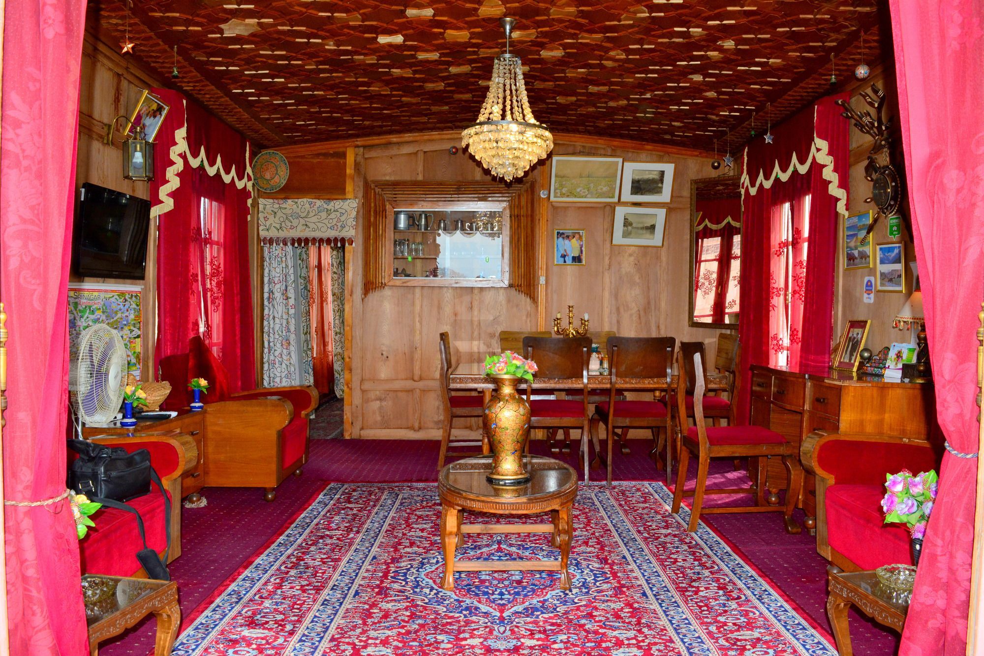 Quarto tradicional com teto de madeira, um candelabro, uma mesa de jantar com cadeiras e um tapete estampado.