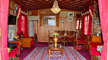 Quarto tradicional com teto de madeira, um candelabro, uma mesa de jantar com cadeiras e um tapete estampado.