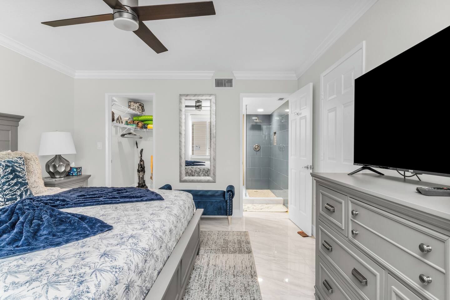 A bedroom with a bed, a television, a dresser, a ceiling fan, and a walk-in closet.