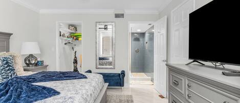A bedroom with a bed, a television, a dresser, a ceiling fan, and a walk-in closet.