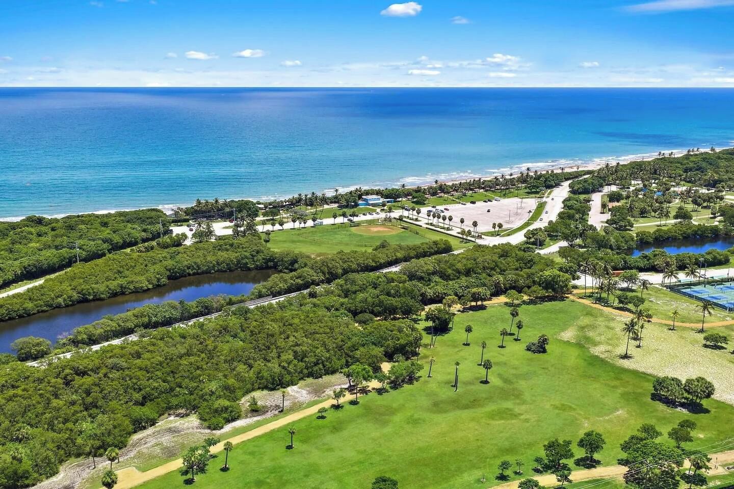 An aerial view of a coastal area with a beach, a golf course, and a large body of water.