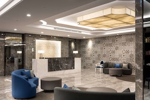 A modern lobby with marble flooring, a reception desk, a blue armchair, a gray sofa, and a patterned wall. - HUA Hotel (Tainan)