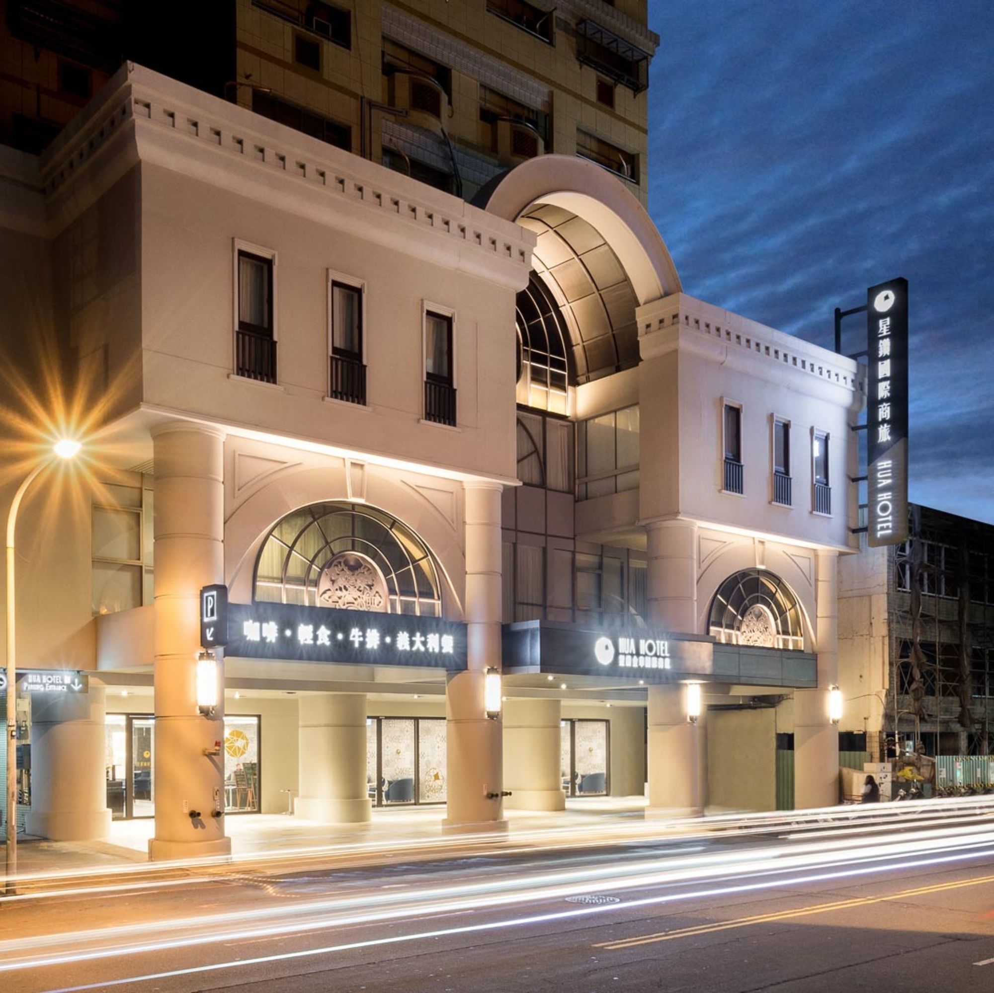 A hotel with a modern facade, large arched windows, and a sign indicating amenities such as dining and a spa.