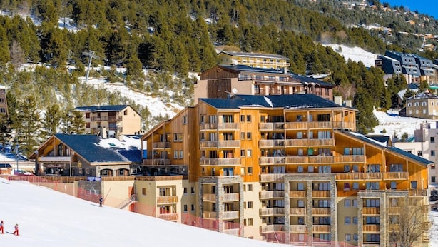 A multi-story hotel with balconies, situated on a snowy slope with a forested hill in the background. - Lagrange L Oree DES Cimes (Les Angles)