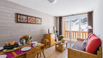 Un coin repas avec une table en bois, des chaises et un buffet. On y trouve également un canapé et une fenêtre donnant sur un paysage enneigé.