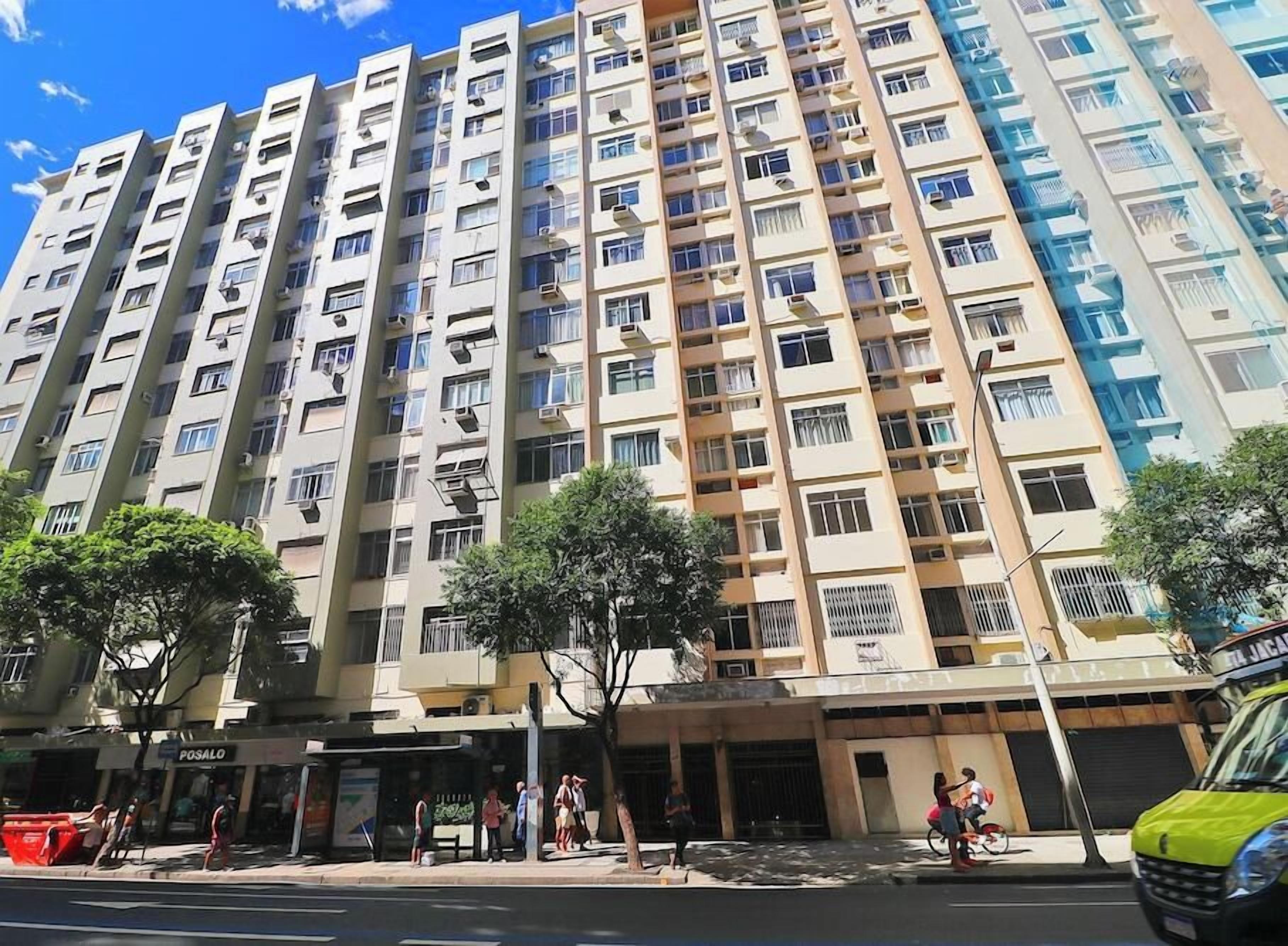 A multi-story residential building with balconies, a visible ground-level commercial space, and a clear sky.