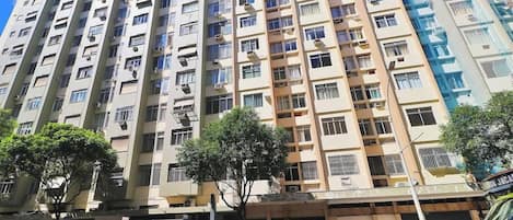 A multi-story residential building with balconies, a visible ground-level commercial space, and a clear sky.