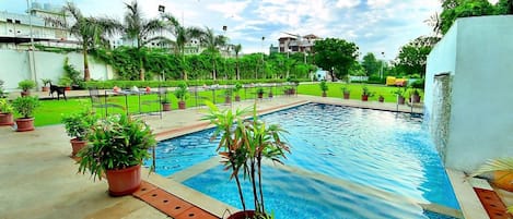 A swimming pool with potted plants, a grassy area, and a clear sky.
