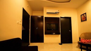 A living room with a sofa, a television, a door, and a wall-mounted air conditioning unit. - V One Pride (Jaipur)