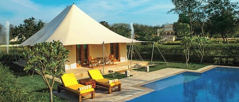 A tented outdoor area with a pool, lounge chairs, and a dining table.