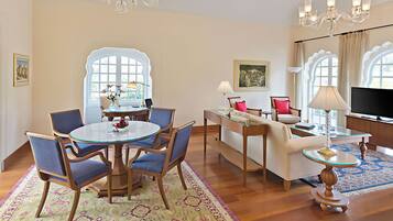 A spacious living room with a round dining table, blue chairs, a sofa, a television, and a chandelier.