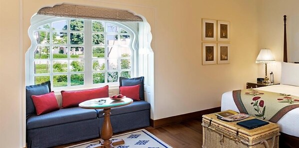 A room with a sofa, a table, a bed, and a window with a view of greenery. - The Oberoi Sukhvilas Spa Resort, New Chandigarh (Kharar)