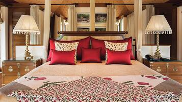 A large bed with a floral bedspread, multiple red and patterned pillows, and two bedside lamps.