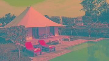 A tented outdoor area with lounge chairs and a pool.