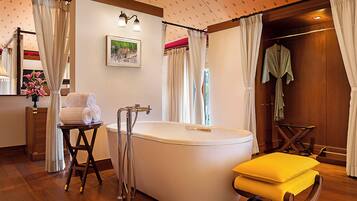 A bathroom with a bathtub, a wooden chair, a towel stand, and a mirror.