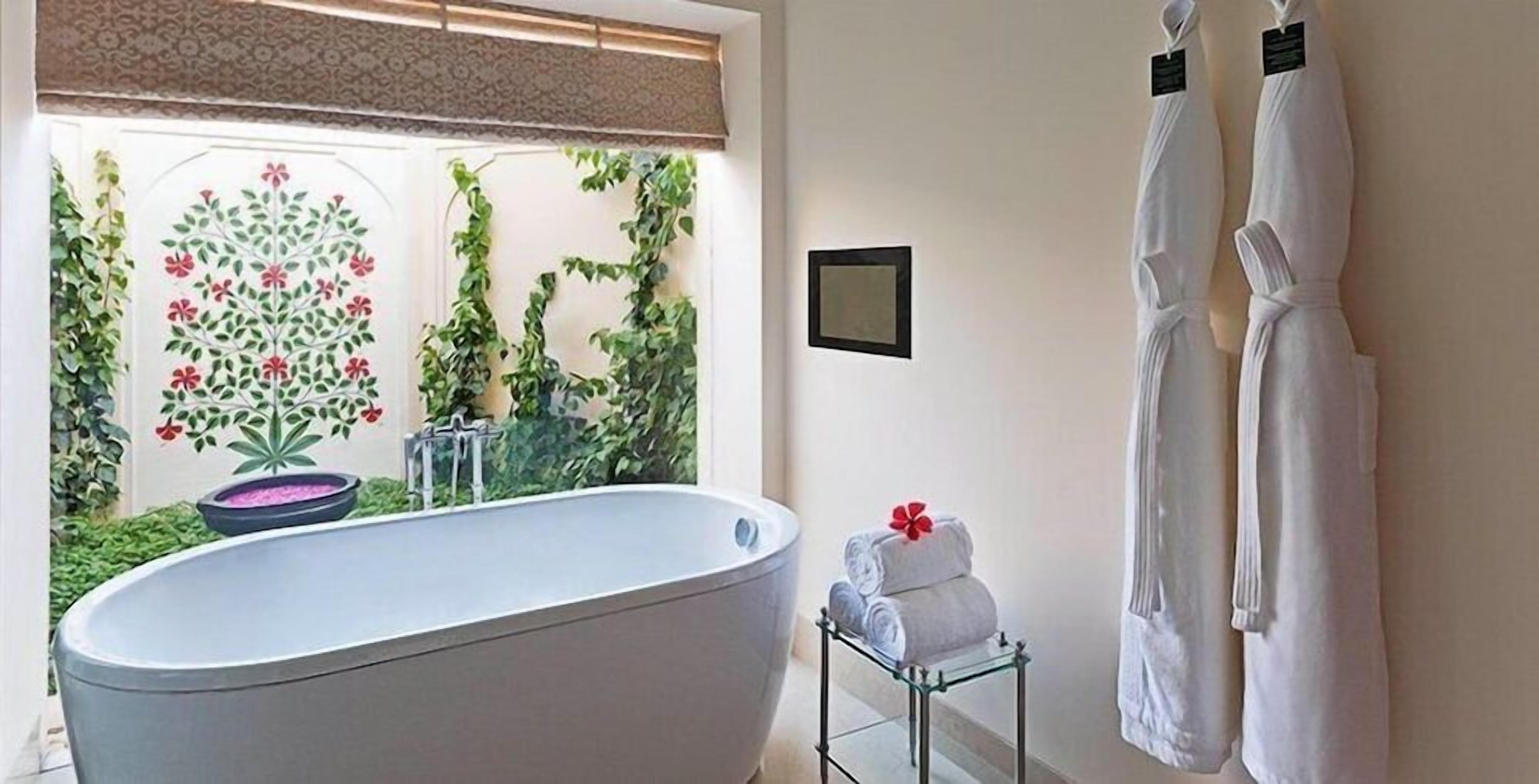A bathroom with a freestanding bathtub, a small table with towels, and a window with a view of greenery.