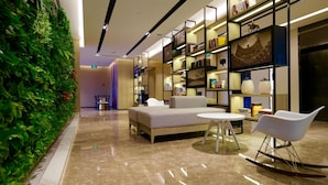 A modern lounge area with a sofa, a round table, and a rocking chair, surrounded by bookshelves and a green wall. - Atour Hotel Tianjin Teda (Tianjin)