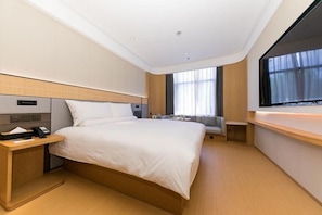 Quarto de hotel com uma cama grande, mesa de cabeceira e televisão fixada na parede.