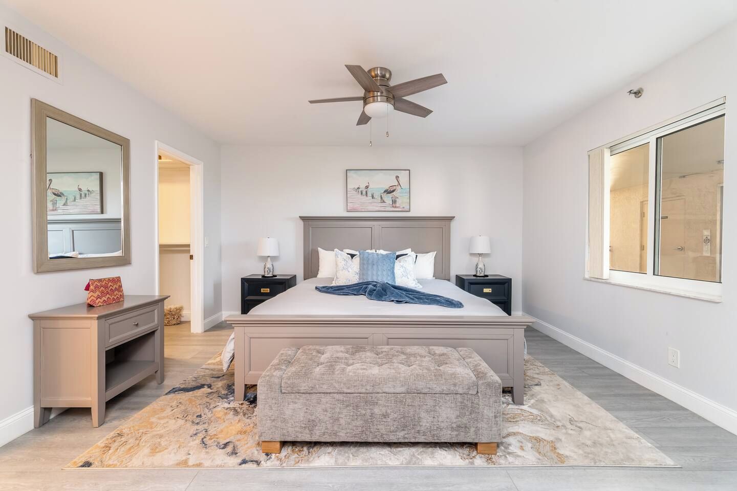 A bedroom with a bed, nightstands, a dresser, a ceiling fan, and a large window.