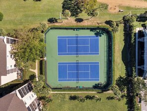 Una vista aerea di un complesso di campi da tennis con due campi, immerso nel verde e circondato da edifici residenziali.