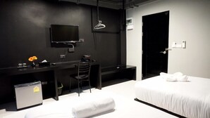 A hotel room with a bed, a desk with a chair, a television, a small trash bin, and a door. - B-black Residence (Chonburi)
