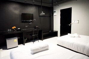 Una habitación de hotel con una cama, un escritorio con una silla, un televisor, un cesto de basura pequeño y una puerta.