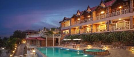 Ein mehrstöckiges Hotel mit Schwimmbad, Außenbereich zum Sitzen und einem Balkon mit Geländern.