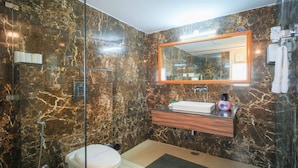 Un baño con pared de mármol, tocador de madera, espejo y un inodoro.