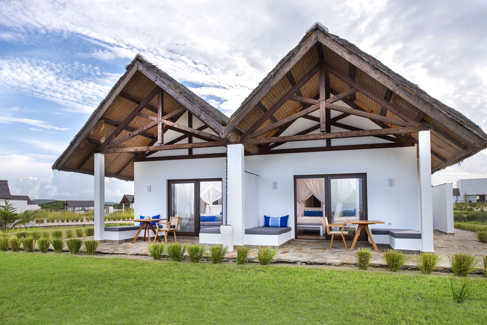 A two-story building with a thatched roof, large windows, and a patio area with seating.