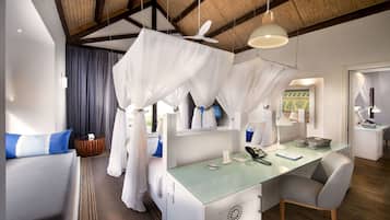 A modern hotel room with a glass desk, a comfortable chair, a bed with white curtains, and a ceiling fan.