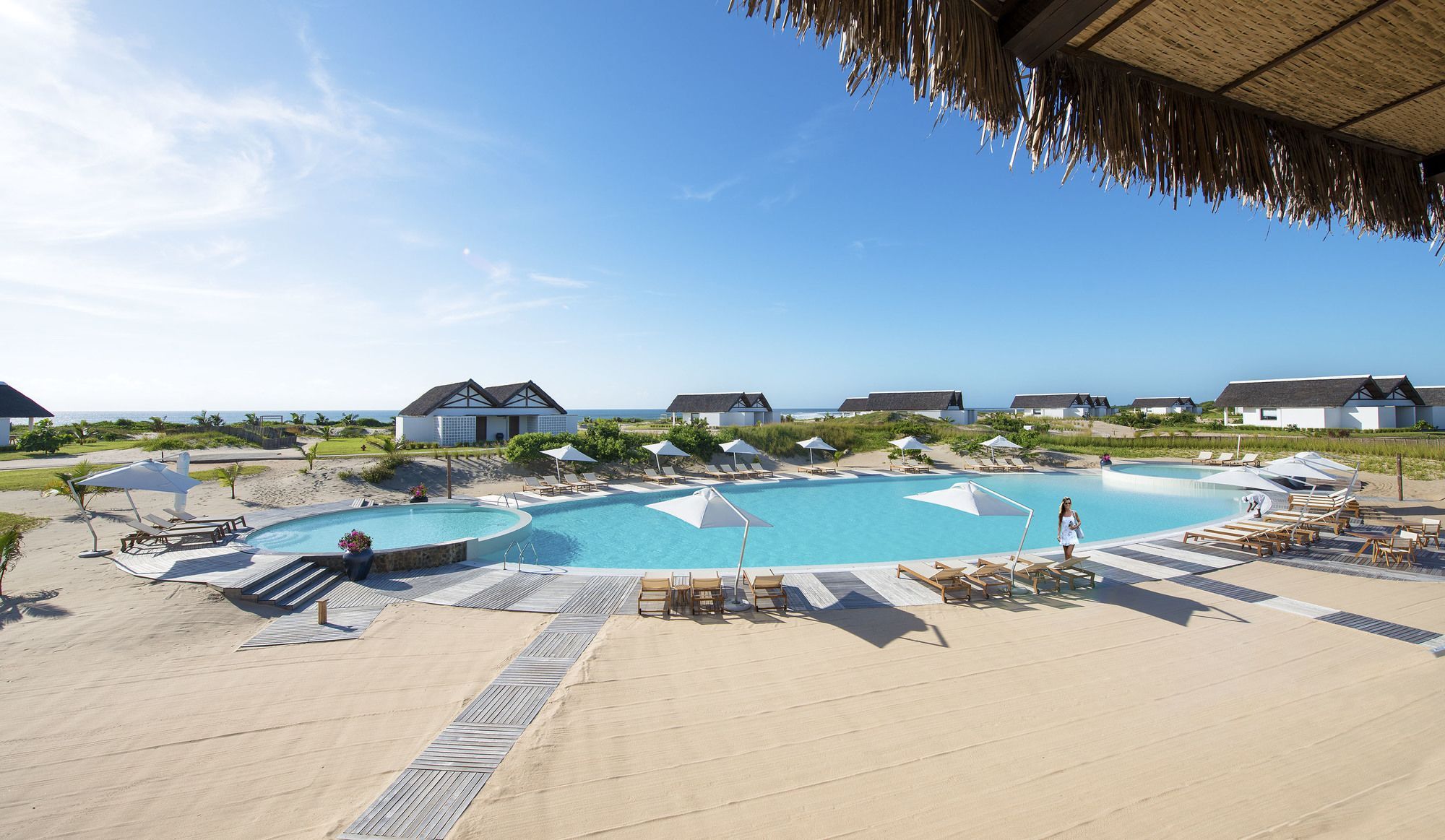A resort with a large pool, lounge chairs, umbrellas, and beach houses.