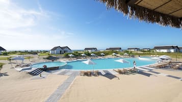 A resort with a large pool, lounge chairs, umbrellas, and beach houses.