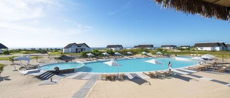 Un resort con una piscina grande, sillas de descanso, sombrillas y casas de playa.