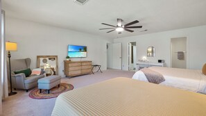 Ein Hotelzimmer mit einem Bett, einem Schreibtisch, einem Sessel, einer Kommode, einem Fernseher und einem Deckenventilator.