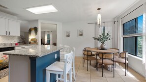 A modern kitchen with a central island, dining area with chairs, and a large window with blinds. - Family stay near Live Oak Park with patio, pool table, & soaker tub (Live Oak)
