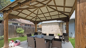 An outdoor patio with a covered seating area, stone wall, and a wooden fence. - Family stay near Live Oak Park with patio, pool table, & soaker tub (Live Oak)