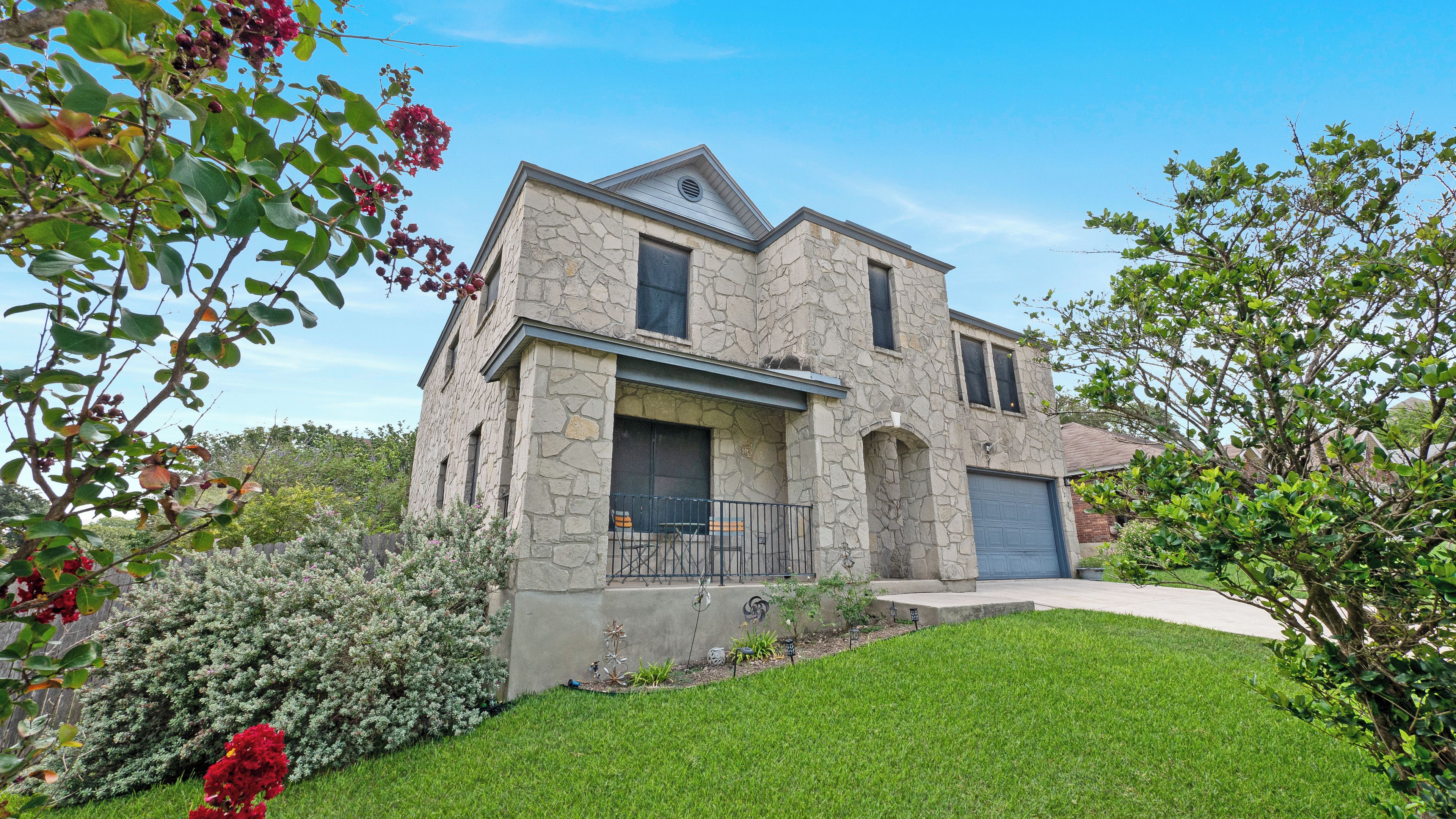 A two-story stone house with a balcony, a garage, and a well-maintained lawn.