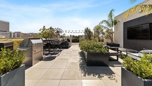 Un patio exterior con una parrilla, asientos y macetas.