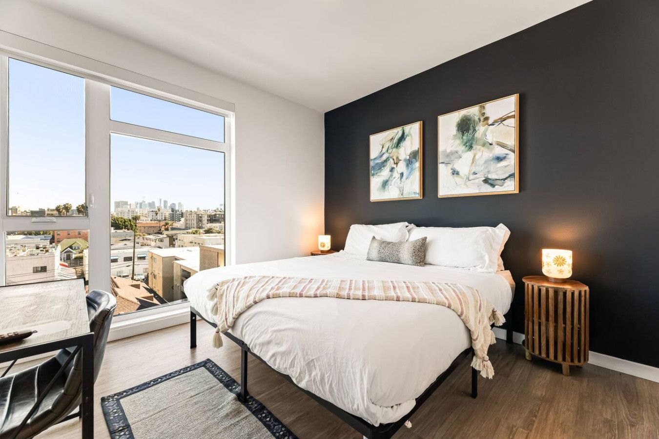 A bedroom with a large bed, two bedside lamps, and a city view.
