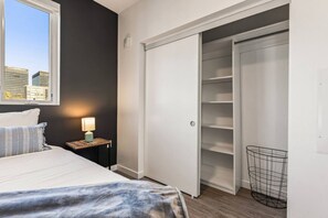 A bedroom with a bed, bedside table with a lamp, a wardrobe, and a view of buildings through a window. - Light-Filled Spacious Executive 2BD+2BTH | Free Parking | Hot tub + Gym (Los Angeles)