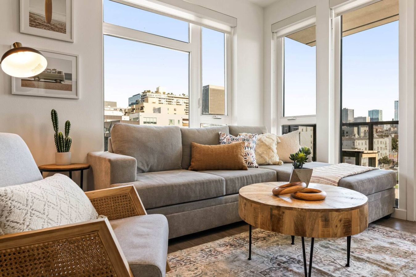 Un salon moderne avec un canapé gris, une table basse ronde en bois et une vue sur la ville grâce à de grandes fenêtres.