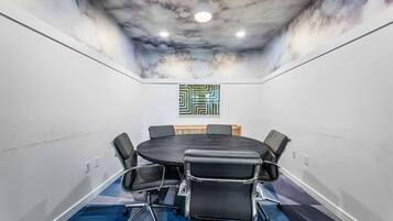 A conference room with a round table, black chairs, a ceiling mural, and a geometric wall art piece.