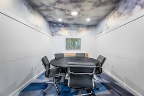 Un salón de conferencias con una mesa redonda, sillas negras, un mural en el techo y una obra de arte geométrica en la pared.