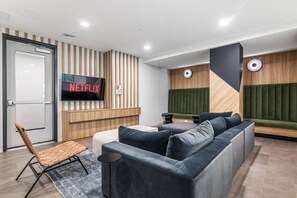 A modern interior with a sectional sofa, a TV screen displaying 'NETFLIX,' and a wooden accent wall. - Light-Filled Spacious Executive 2BD+2BTH | Free Parking | Hot tub + Gym (Los Angeles)
