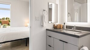 Habitación de hotel moderna con cama, baño con espejo grande, lavabo y vistas a la ciudad.