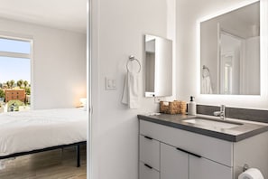 Ein modernes Hotelzimmer mit Bett, Badezimmer mit großem Spiegel, Waschbecken und Blick auf die Stadt.