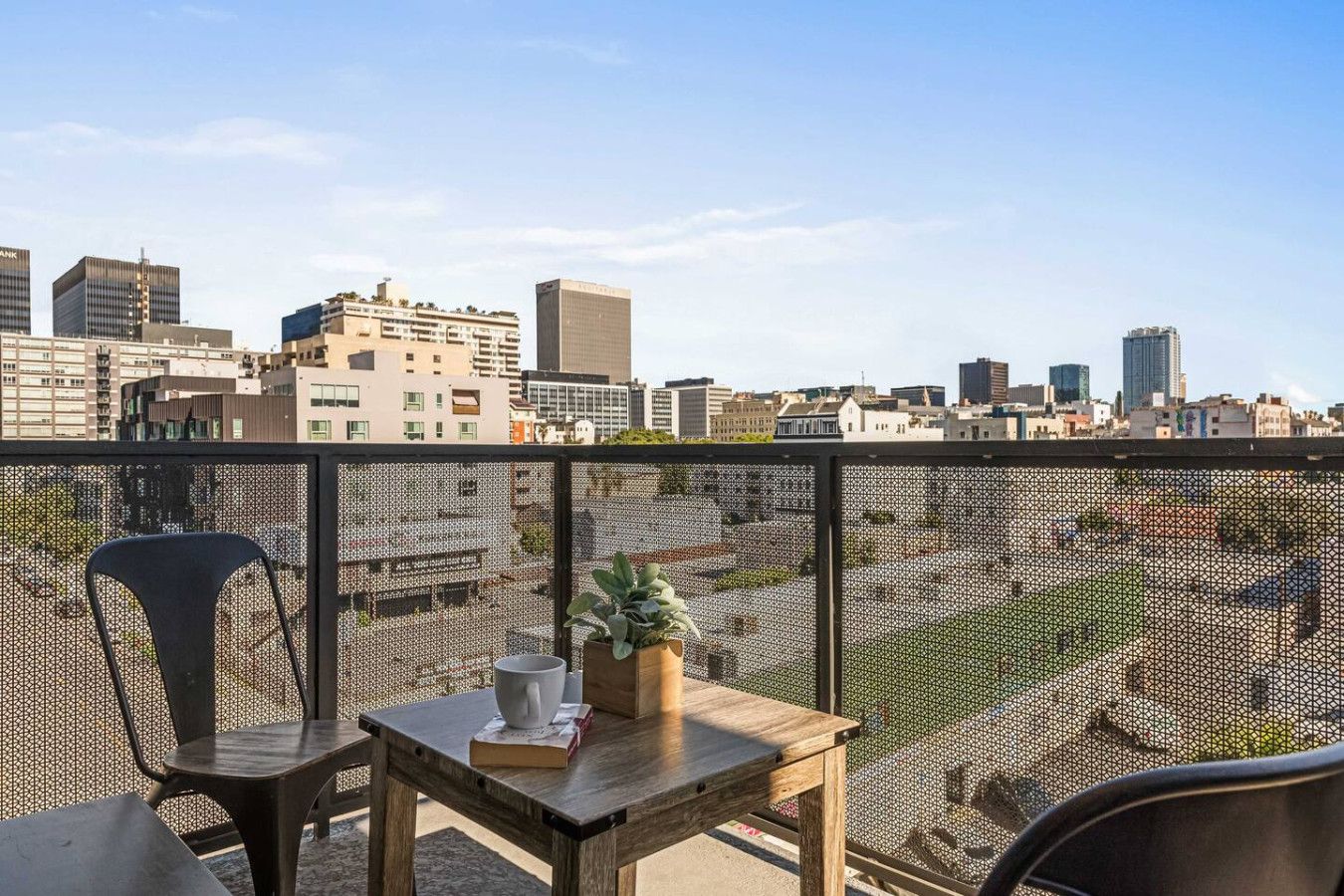 Un balcon offrant une vue sur le paysage urbain, avec une table agrémentée d’une plante, une chaise et un livre.