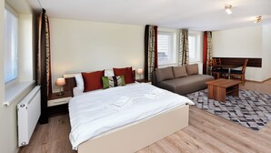 A bedroom with a large bed, a sofa, a small table, and a window with curtains. - Resort Beatrice Depandance Julia (Vysoké Tatry)
