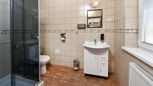 A bathroom with a glass shower enclosure, a toilet, a sink with a mirror, and a waste bin. - Resort Beatrice Depandance Julia (Vysoké Tatry)