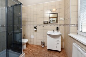 A bathroom with a glass shower enclosure, a toilet, a sink with a mirror, and a waste bin. - Resort Beatrice Depandance Julia (Vysoké Tatry)